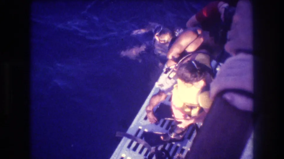 Overhead view of a child in a yellow life vest on a boat boarding platform at night, Acapulco, Mexico, circa 1982, shot on 8mm home movie film.