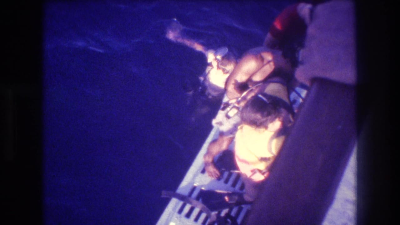 Overhead shot of a child in a yellow life vest at a grated boat stern platform at night, Acapulco, Mexico, circa 1982, 8mm home movie.