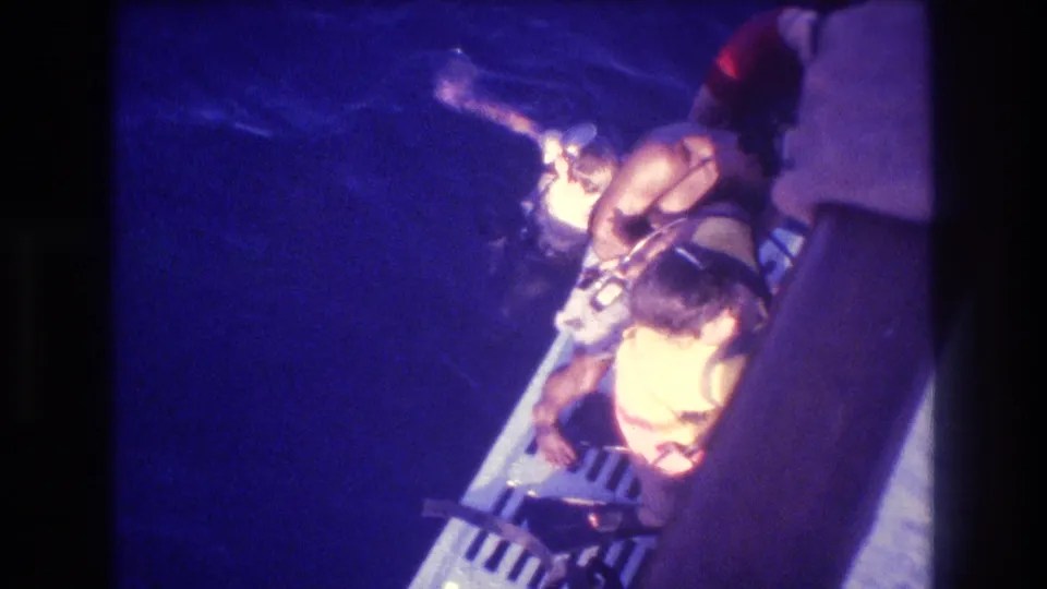 Overhead shot of a child in a yellow life vest at a grated boat stern platform at night, Acapulco, Mexico, circa 1982, 8mm home movie.