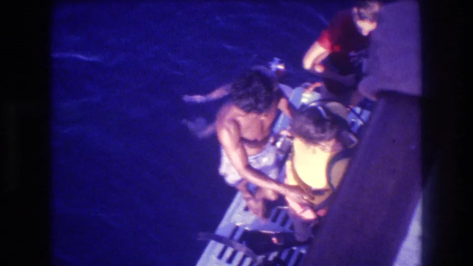 Overhead view of a child in a yellow life vest at a boat platform edge at night, Acapulco, Mexico, circa 1982, 8mm home movie.
