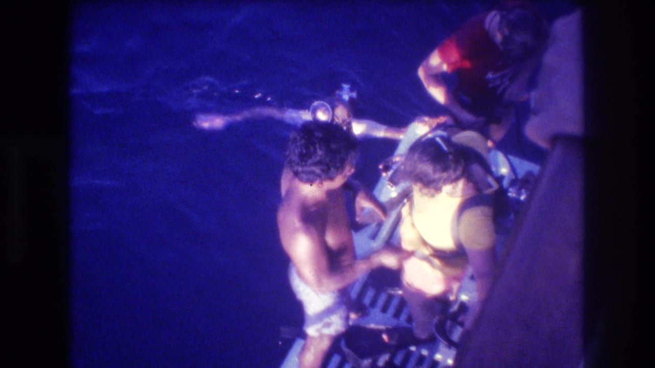 Close overhead view of shirtless man and diver in yellow top with scuba equipment on night boat deck.