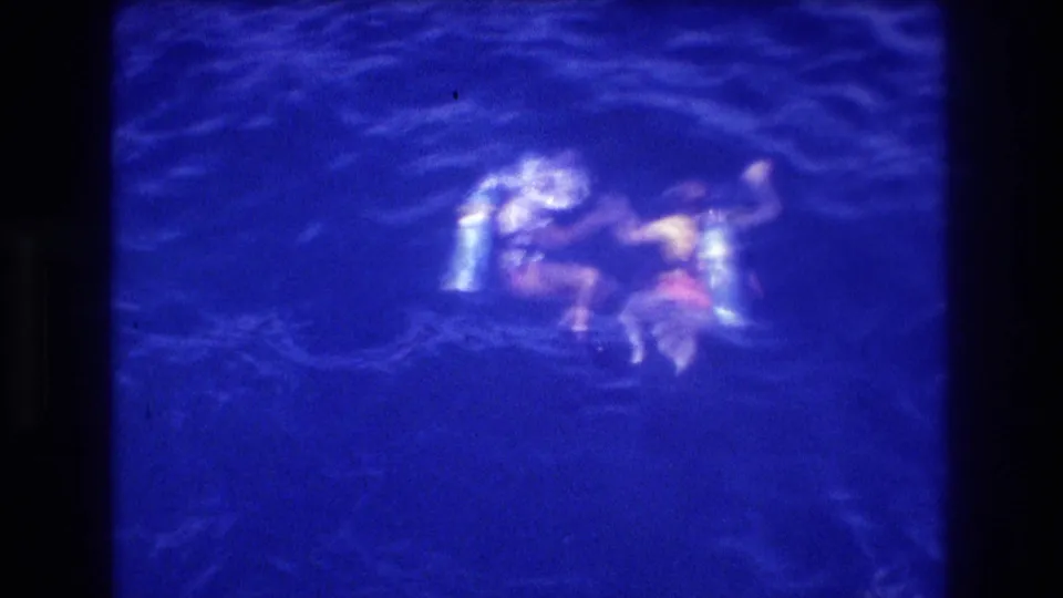 Bird's-eye view of diver in dark ocean water at night, Acapulco Mexico ca. 1982, figure drifts from boat in light-coloured top under artificial illumination.
