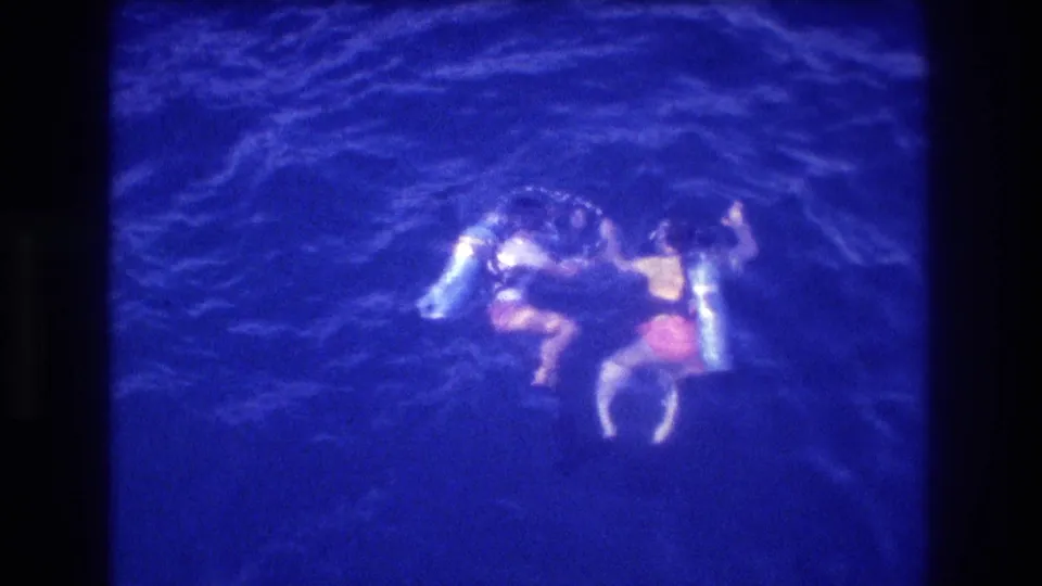 Two scuba divers on the surface of the ocean near Acapulco, Mexico, circa 1982, captured on 8mm film from an elevated angle above.