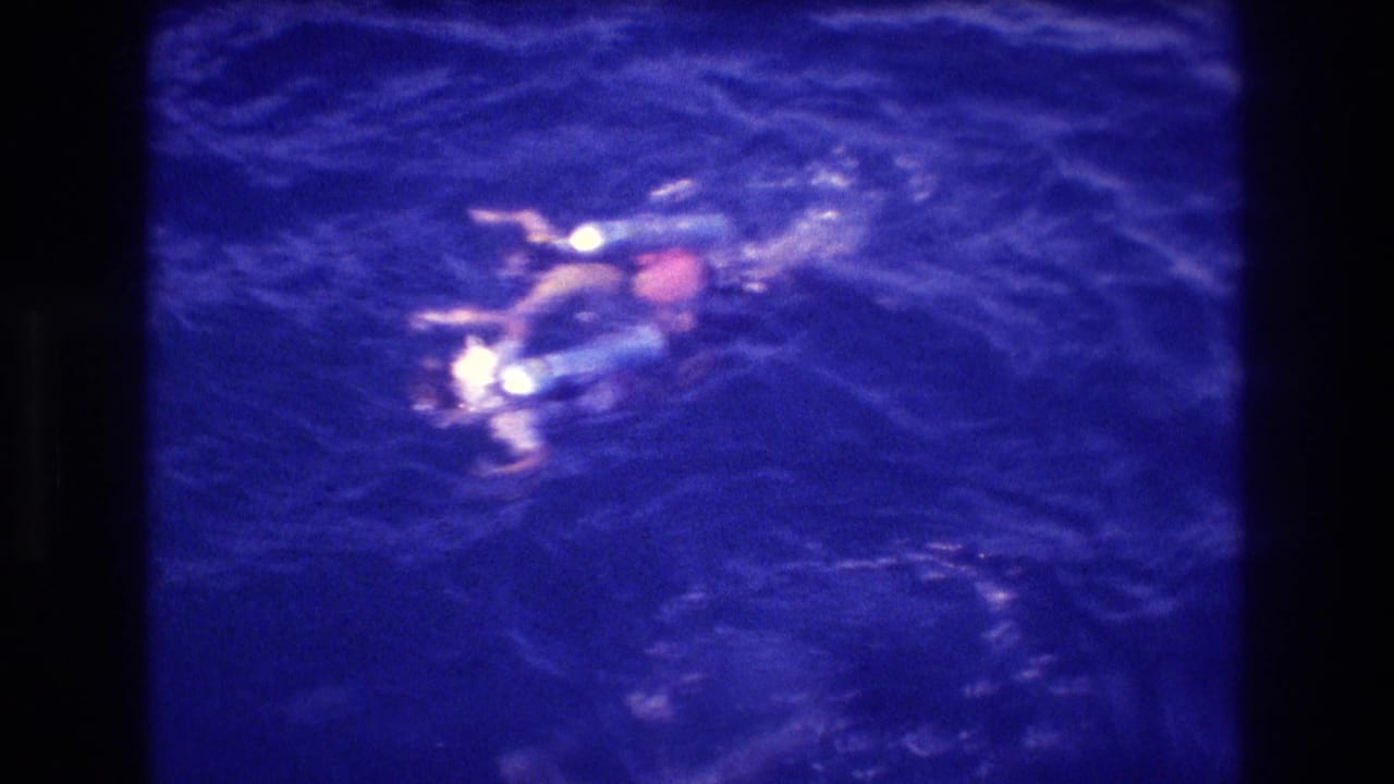 Two swimmers with blue snorkeling equipment and red-orange swimwear at ocean surface, filmed from above, likely Acapulco, Mexico, circa 1982.