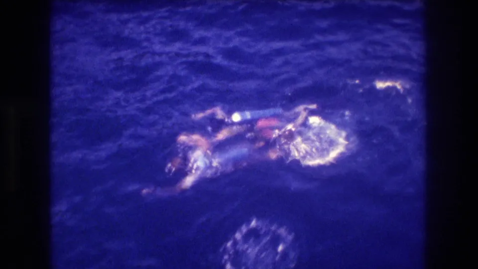 Swimmer or swimmers with blue equipment and red-orange swimwear in deep blue ocean viewed from above, consistent with 1982 Acapulco vacation footage.