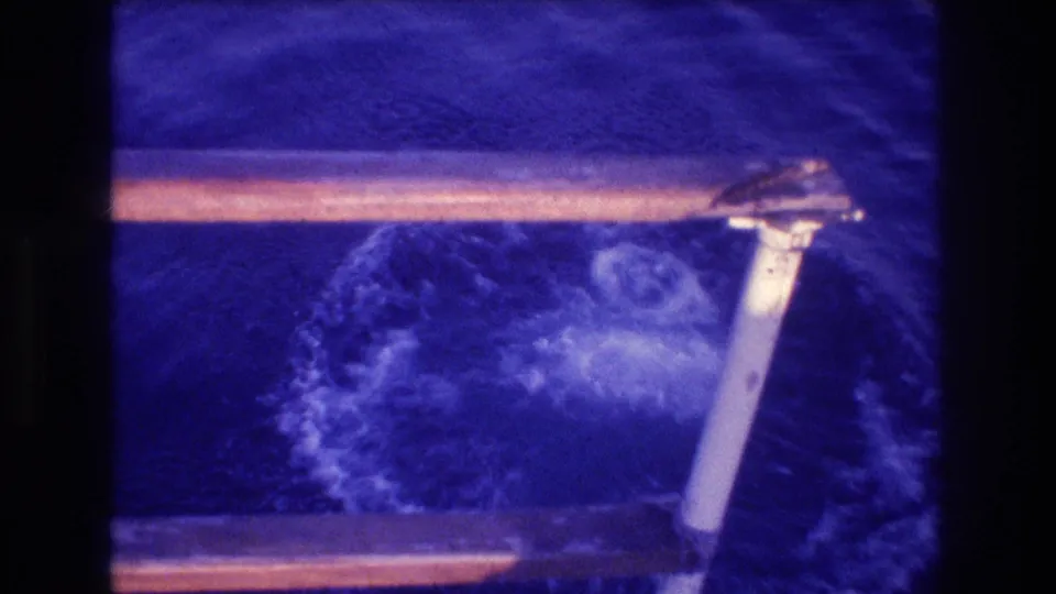8mm home-movie frame of a wood-and-metal boat railing in the foreground with churning water and bubbles beneath; Acapulco area, 1982.