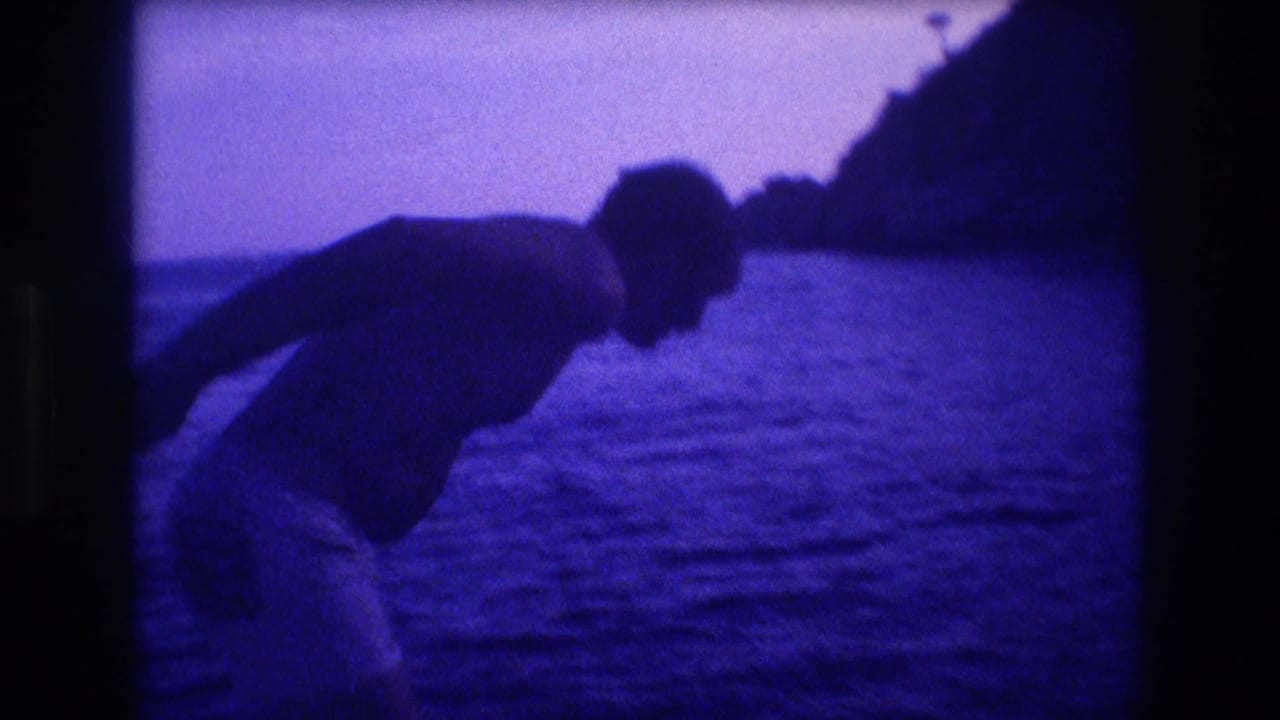 Man in dark swim shorts crouching to dive, rocky cliff silhouette at right, pale violet sky