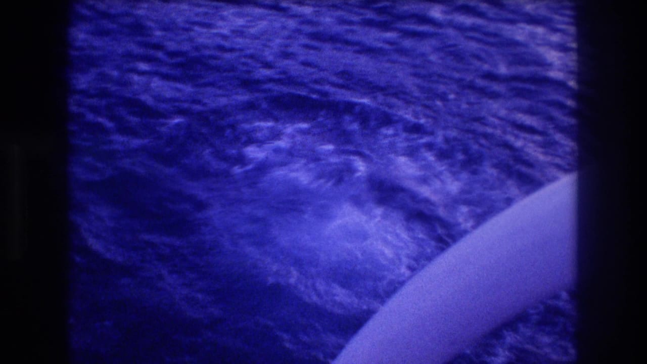 Blue-toned 8mm shot of choppy ocean surface with white boat hull edge at lower frame.