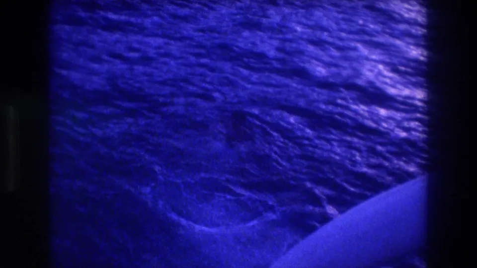 8mm home-movie frame of ocean surface from boat deck, circa 1982 Acapulco; deep blue-purple film cast with grain and water ripples visible.