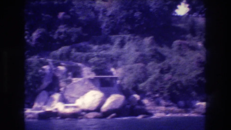 Boulders and lush tropical vegetation along the Acapulco shoreline with calm ocean water at the base, 8mm home movie from 1982.