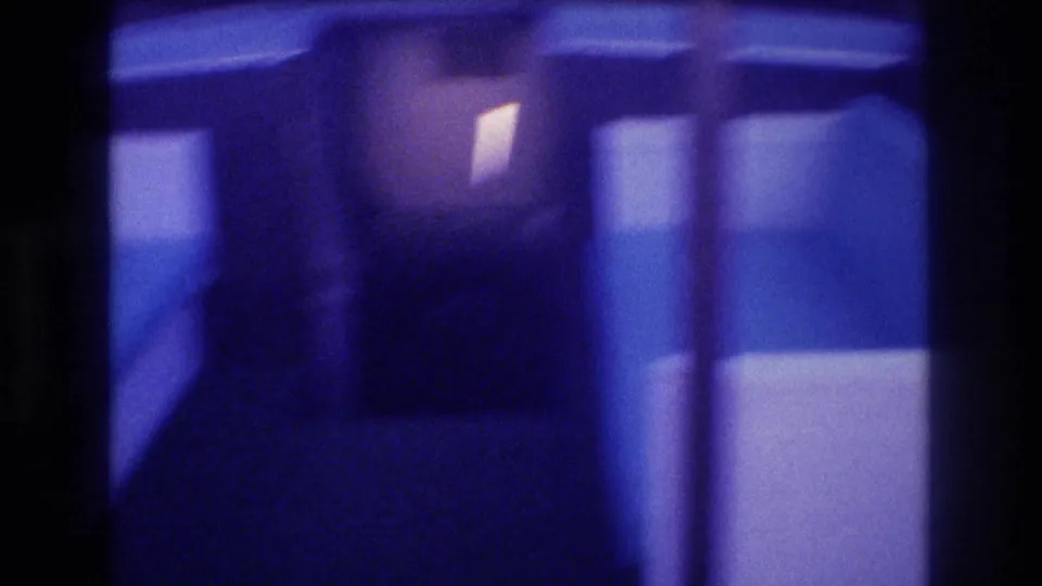 Transitional frame from a 1982 8mm home movie: boat interior during camera pan with heavy motion blur and blue-purple color cast.