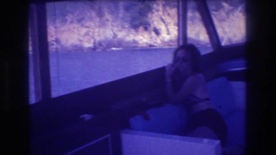 Woman relaxing in boat cabin identified in clip title as Acapulco, Mexico, 1982; rocky coastal cliffs visible through windows; heavy blue-violet tint from aged 8mm film.