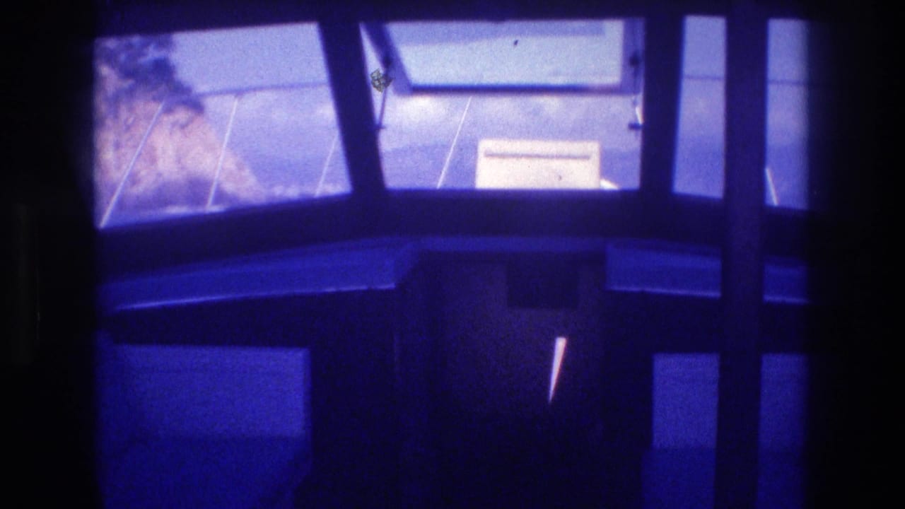 Boat cabin interior, possibly Acapulco, Mexico, 1982; rocky cliffs and a partially visible sign or notice through windows; pronounced blue-violet 8mm color shift.