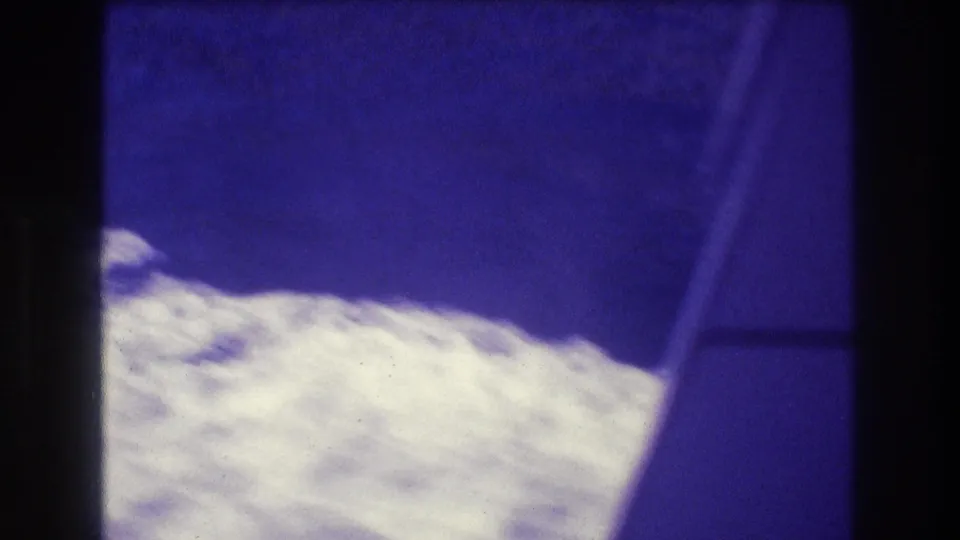 Underexposed 8mm frame from inside a moving speedboat showing a diagonal window frame or rail and white churned water below, Acapulco 1982.