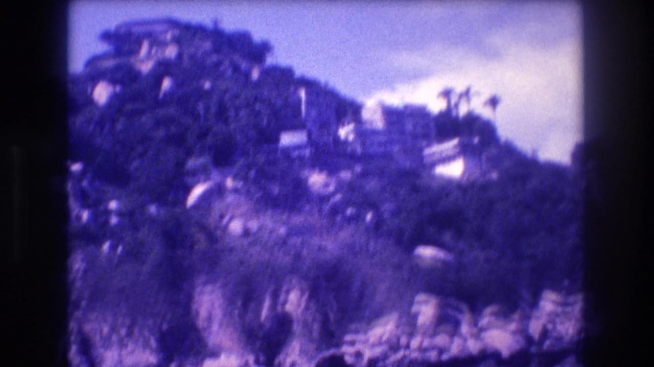Steep vegetated cliff above Acapulco Bay, ca. 1982, with what appear to be villas at the crest; 8mm footage with heavy blue-purple color cast.