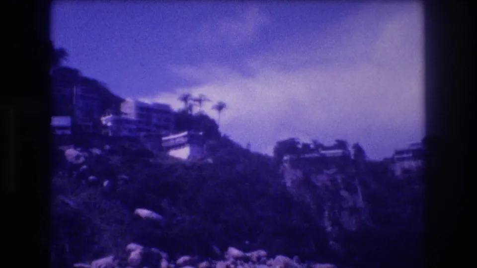 Acapulco clifftop buildings and palm trees seen across the bay, ca. 1982, on 8mm film with visible grain and blue-purple color shift.