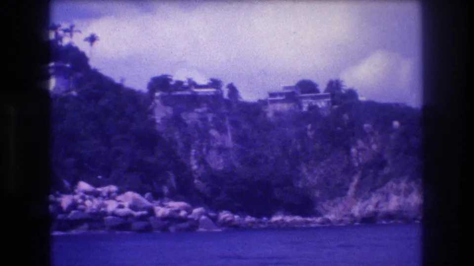 Rocky Acapulco Bay headland with clifftop structures and large boulders at the waterline, ca. 1982; 8mm home movie with characteristic color drift.