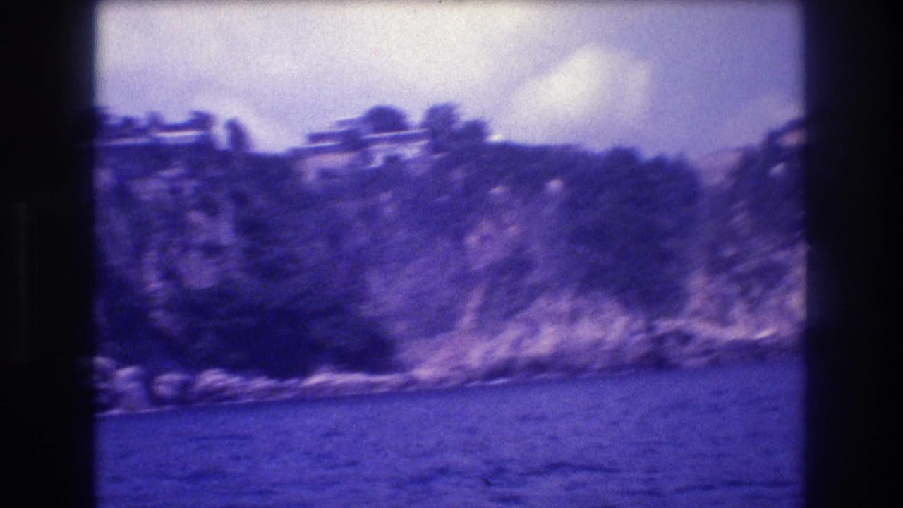 8mm footage from a moving boat showing vegetation-covered cliff with light-colored structures at summit, Acapulco coastline, circa 1982.
