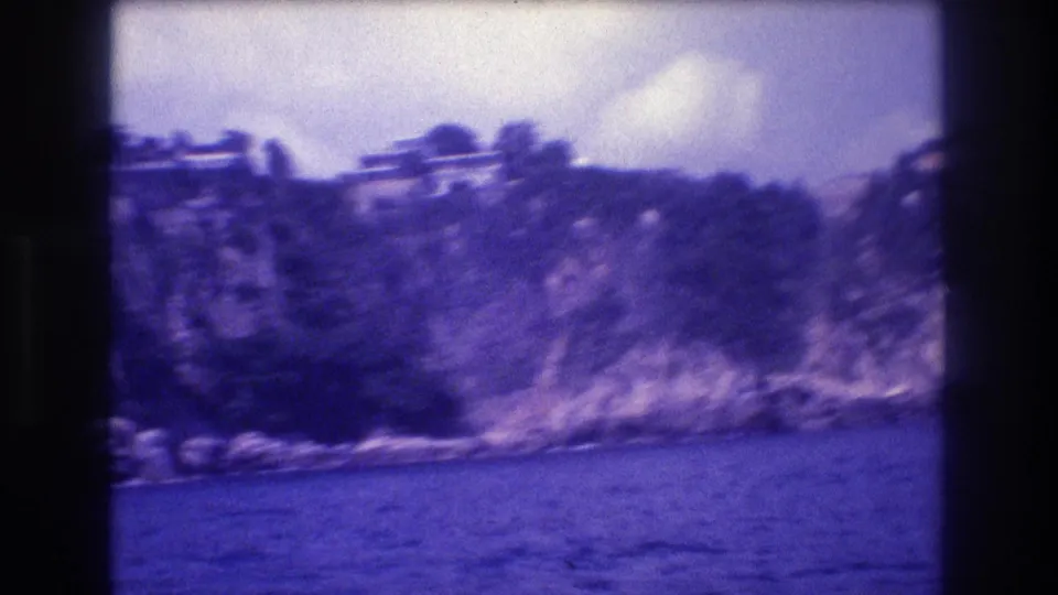 8mm footage from a moving boat showing vegetation-covered cliff with light-colored structures at summit, Acapulco coastline, circa 1982.