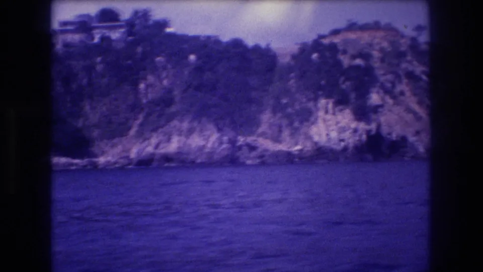 8mm home movie frame showing a rocky forested headland on what the metadata identifies as the Acapulco coast, Mexico, 1982, with heavy purple color shift from aged film.