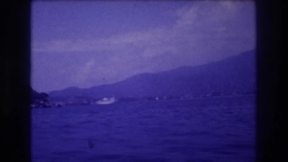 8mm home movie frame panning across Acapulco bay, Mexico, circa 1982, showing a hazy mountain ridge, open water, and a distant white motorboat.