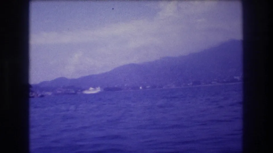 Final 8mm frame of a boat-shot coastal pan near Acapulco, Mexico, 1982, showing a low mountain ridge and a small white motorboat on the bay.