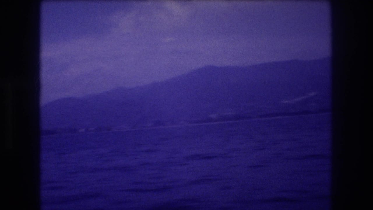 8mm home movie frame circa 1982 showing open ocean and a mountain ridge with strong violet dye-shift, likely Acapulco, Mexico.