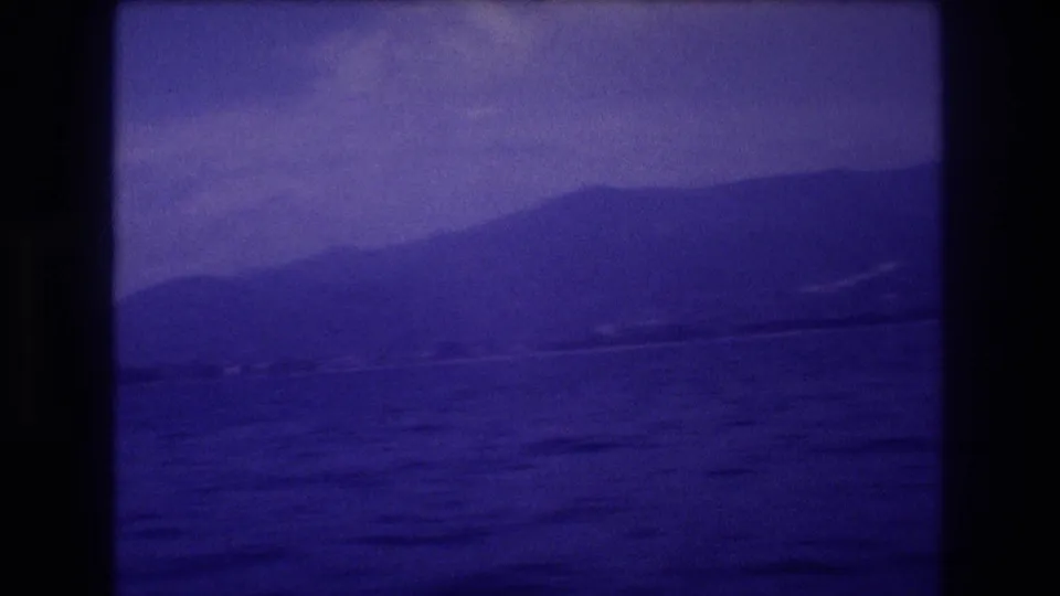8mm home movie frame circa 1982 showing open ocean and a mountain ridge with strong violet dye-shift, likely Acapulco, Mexico.