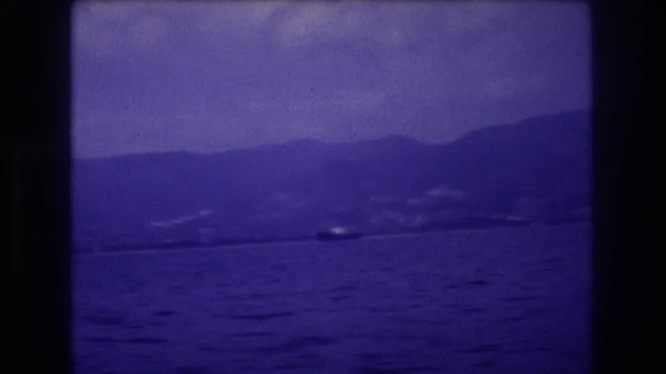 8mm home movie frame circa 1982 showing ocean surface, distant mountain ridge, and a possible small boat in mid-distance, likely Acapulco, Mexico.