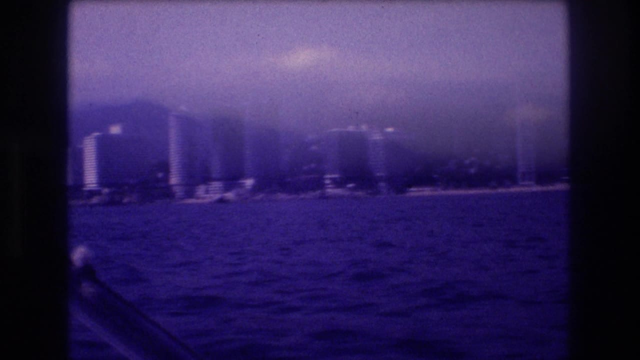 Cluster of tall hotel towers along Acapulco's waterfront seen from a boat, rugged mountains behind, dark choppy ocean in foreground.