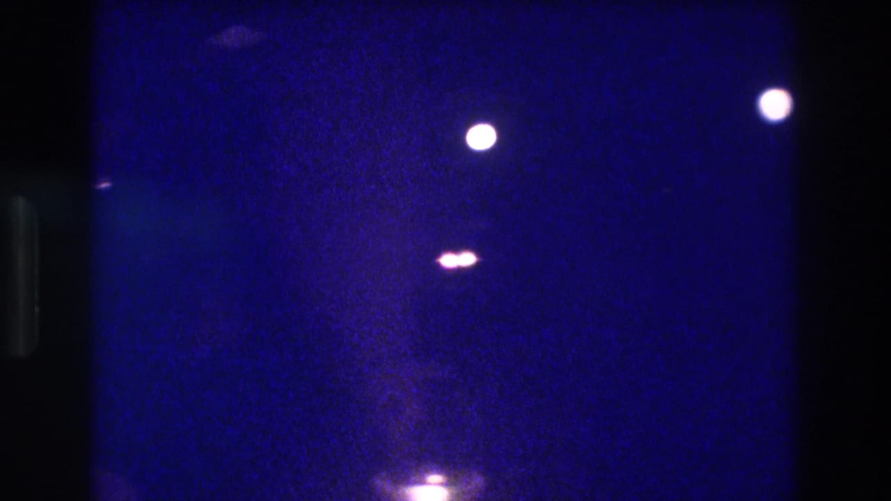 Underexposed 8mm home movie frame circa 1982 showing scattered point lights and a diffuse bottom glow against heavy blue film grain, location asserted as Acapulco by metadata.