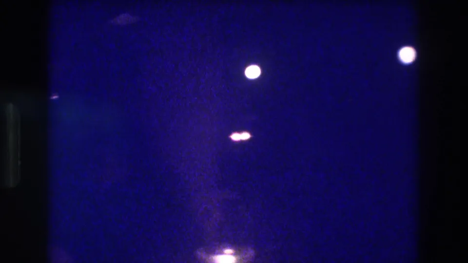 Underexposed 8mm home movie frame circa 1982 showing scattered point lights and a diffuse bottom glow against heavy blue film grain, location asserted as Acapulco by metadata.