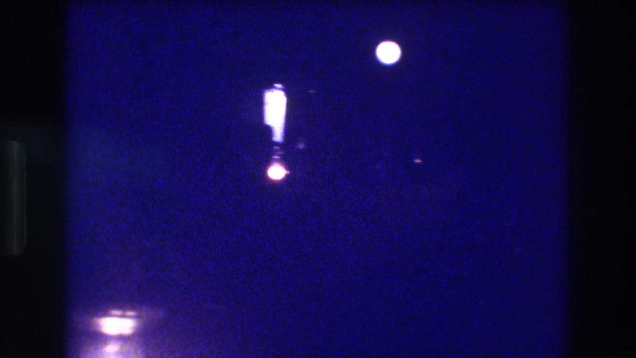 8mm night frame with a large white orb upper-right, an elongated vertical luminous shape center, a warm pink-orange glow beneath it, and a horizontal light band at the bottom.
