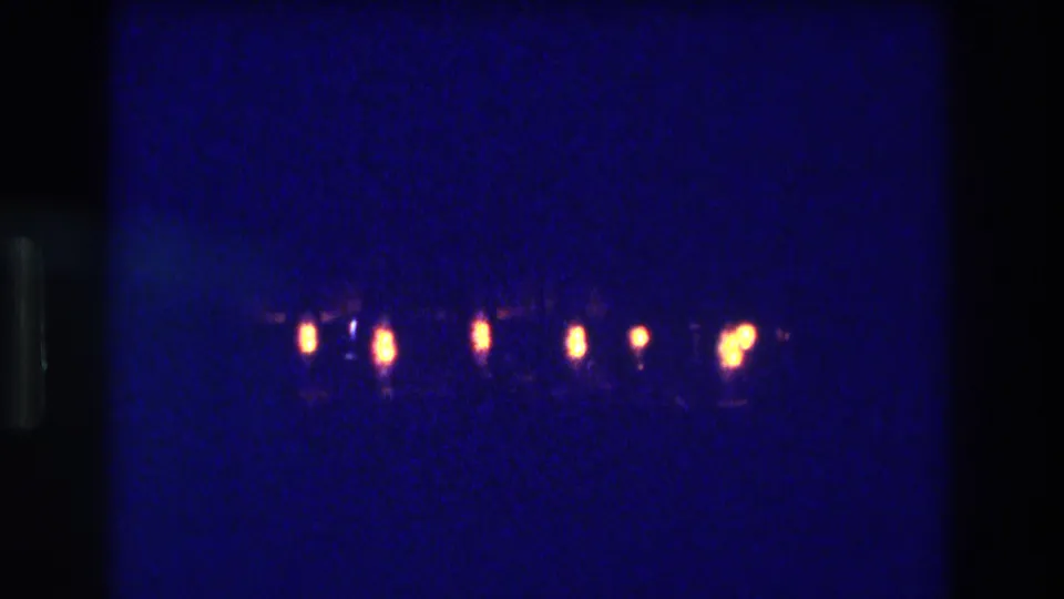 8mm home-movie frame from an Acapulco 1982 performance, showing a row of warm amber stage or footlights along the bottom against a dark background with visible film grain.