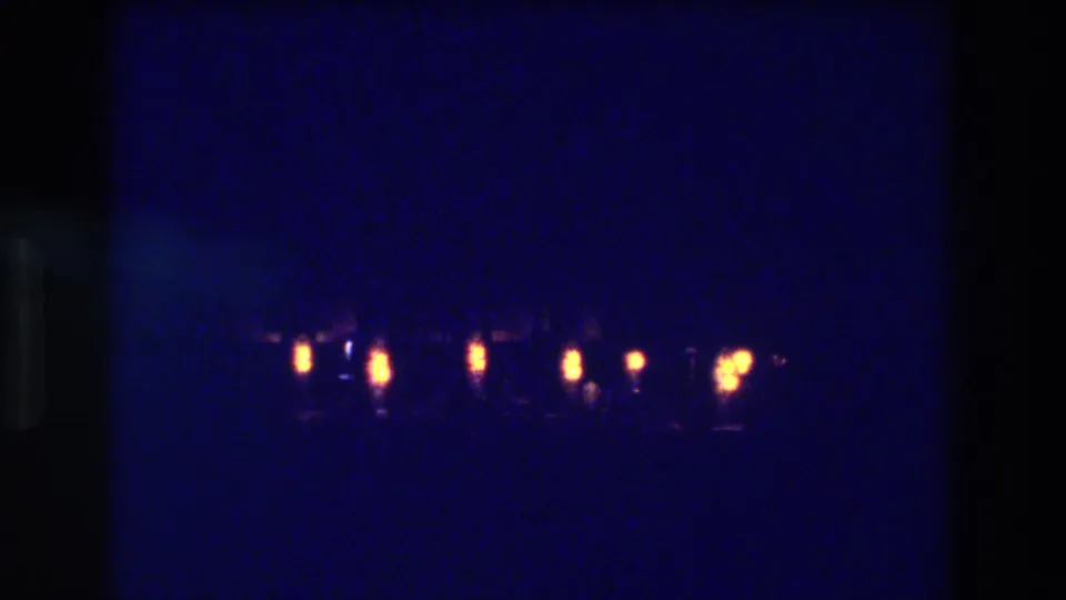 8mm home-movie frame from an Acapulco 1982 performance, showing a row of amber lights at the bottom with a residual blue cast in the upper field and visible analog film grain.