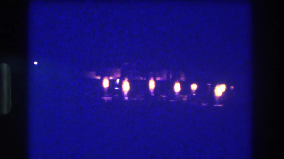 8mm home-movie frame circa 1982, Acapulco, Mexico — a row of amber lights and their shimmering water reflections spread across the lower frame.