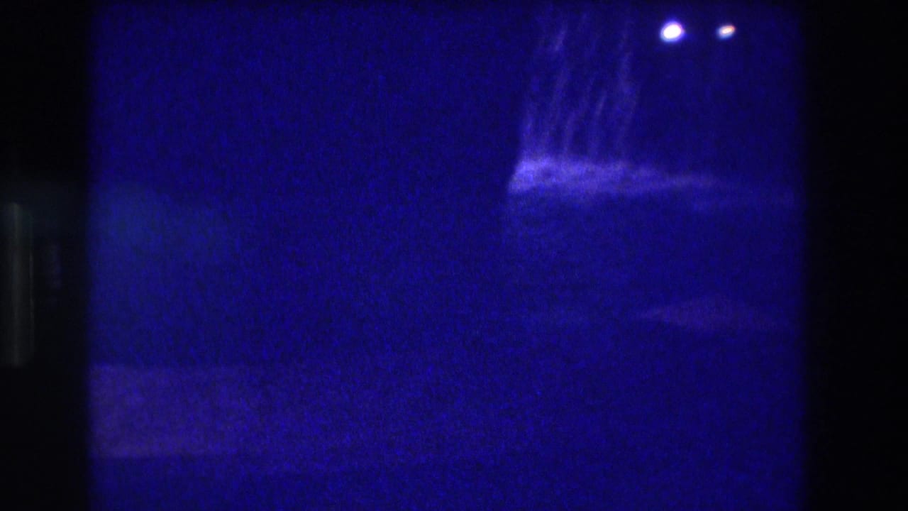 8mm home movie frame from Acapulco, 1982 — camera repositions, leaving a largely dark blue field with the cascade and distant lights at upper right, strong light leak at left edge.