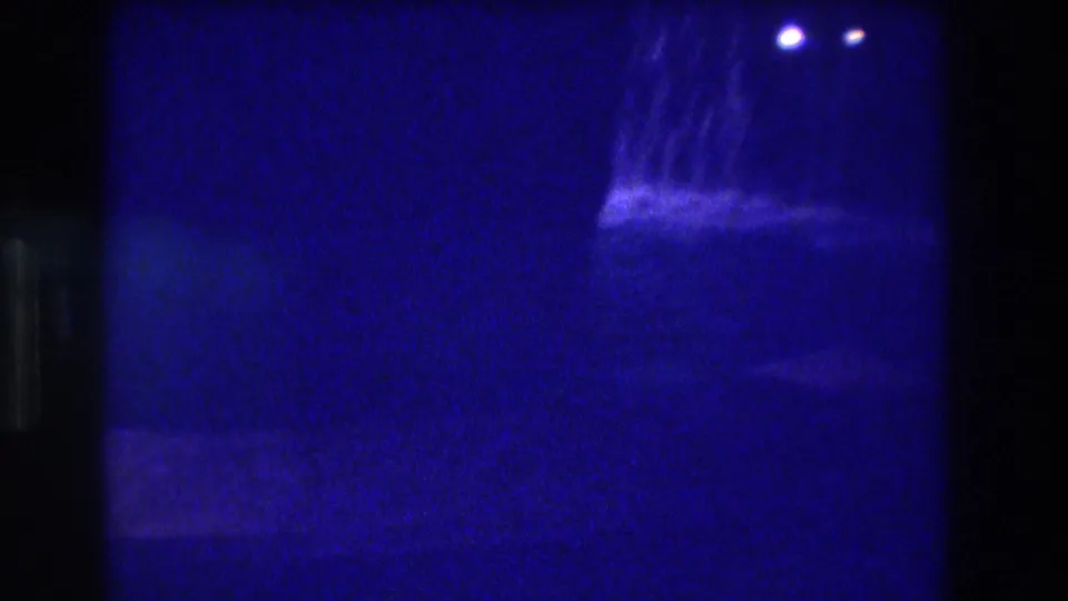 8mm home movie frame from Acapulco, 1982 — camera repositions, leaving a largely dark blue field with the cascade and distant lights at upper right, strong light leak at left edge.