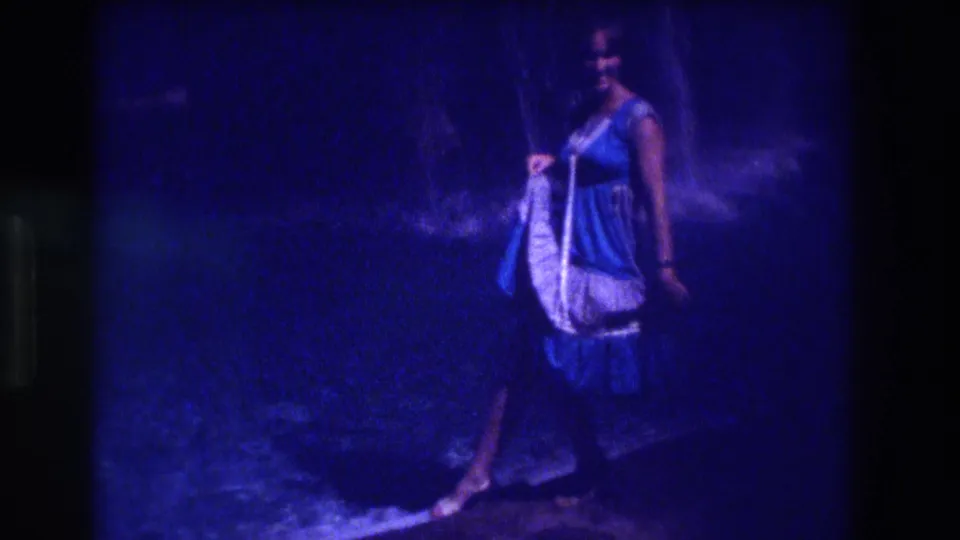 Side view of woman in blue and white dress holding a white garment, 8mm home movie, Acapulco, Mexico, circa 1982, nighttime outdoor setting.