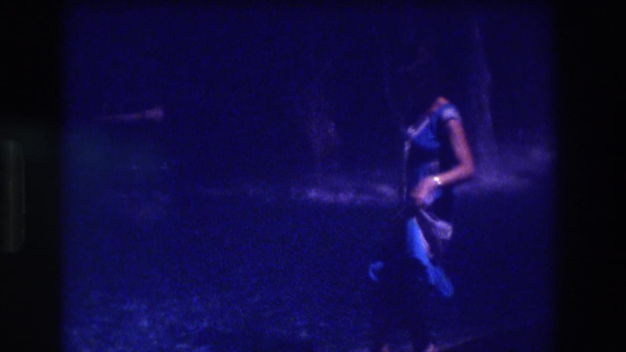 Woman in blue dress in motion against a dark background, partially visible in profile, with strong blue color cast and film grain.