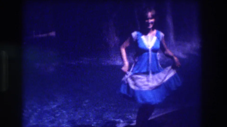 Smiling woman in blue and white dress dancing and facing camera, 8mm home movie, Acapulco, Mexico, circa 1982, nighttime beach setting.