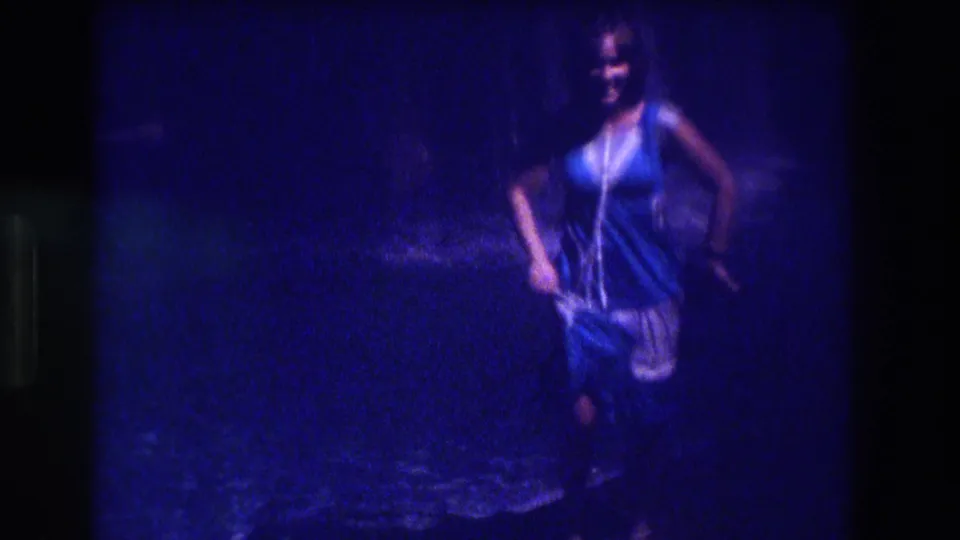 Woman in blue and white dress posing and smiling, three-quarter view, 8mm home movie, Acapulco, Mexico, circa 1982, nighttime outdoor setting.