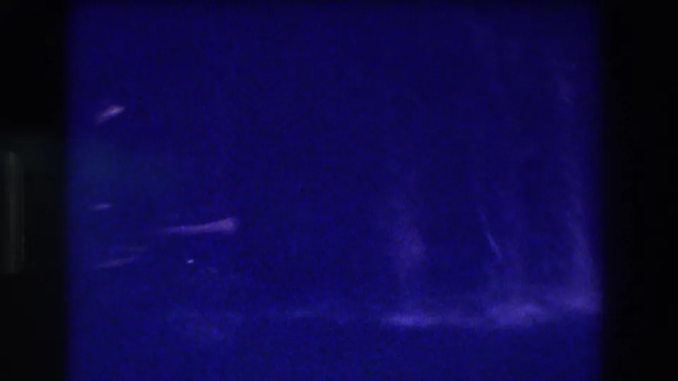 Severely underexposed 8mm frame with faint water or wet-surface traces and extreme blue cast, from waterfall footage likely shot in Acapulco circa 1982.