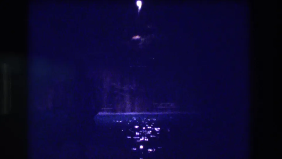 Closing frame of apparent 1982 Acapulco night sequence — solitary point-light and wet-ground reflections persist in deep blue, grain-heavy 8mm field