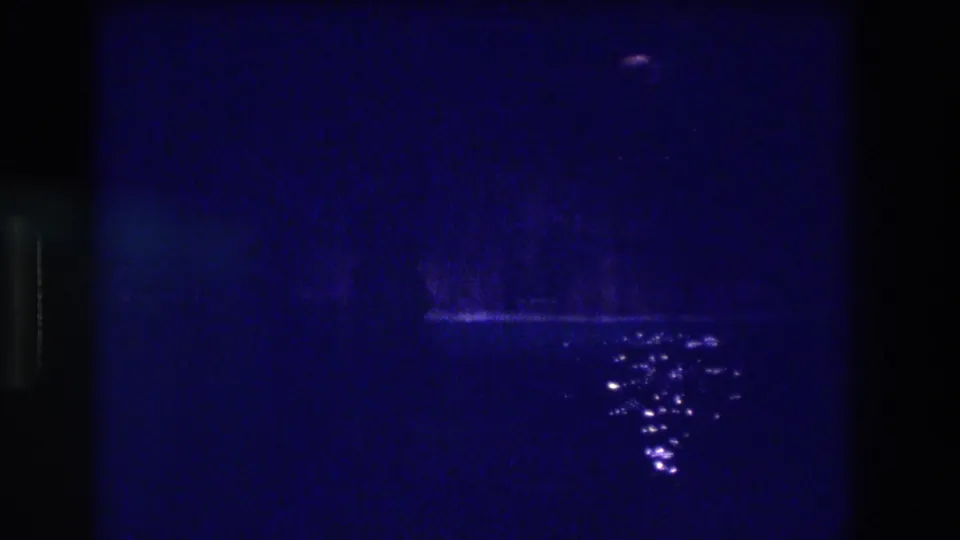 Night pool scene on 8mm, circa 1982, Acapulco, Mexico — deep blue darkness with glinting water surface reflections and a faint upper light.