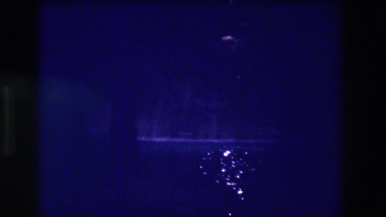 Continuation of the Acapulco 1982 night pool sequence on 8mm — blue field with shifting specular glints on dark water.