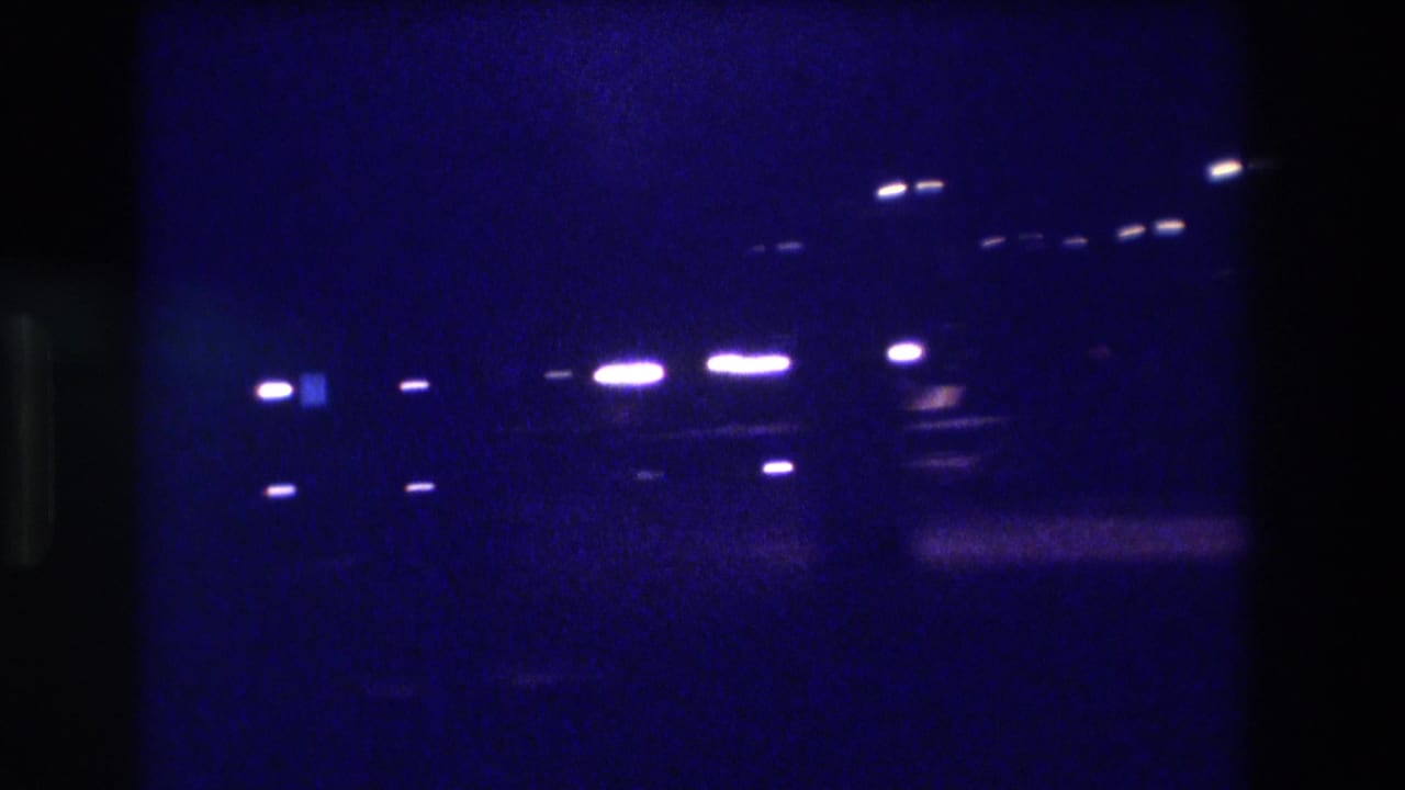 Cluster of bright white light points against deep blue darkness, possibly overhead street lamps or parking area lights.