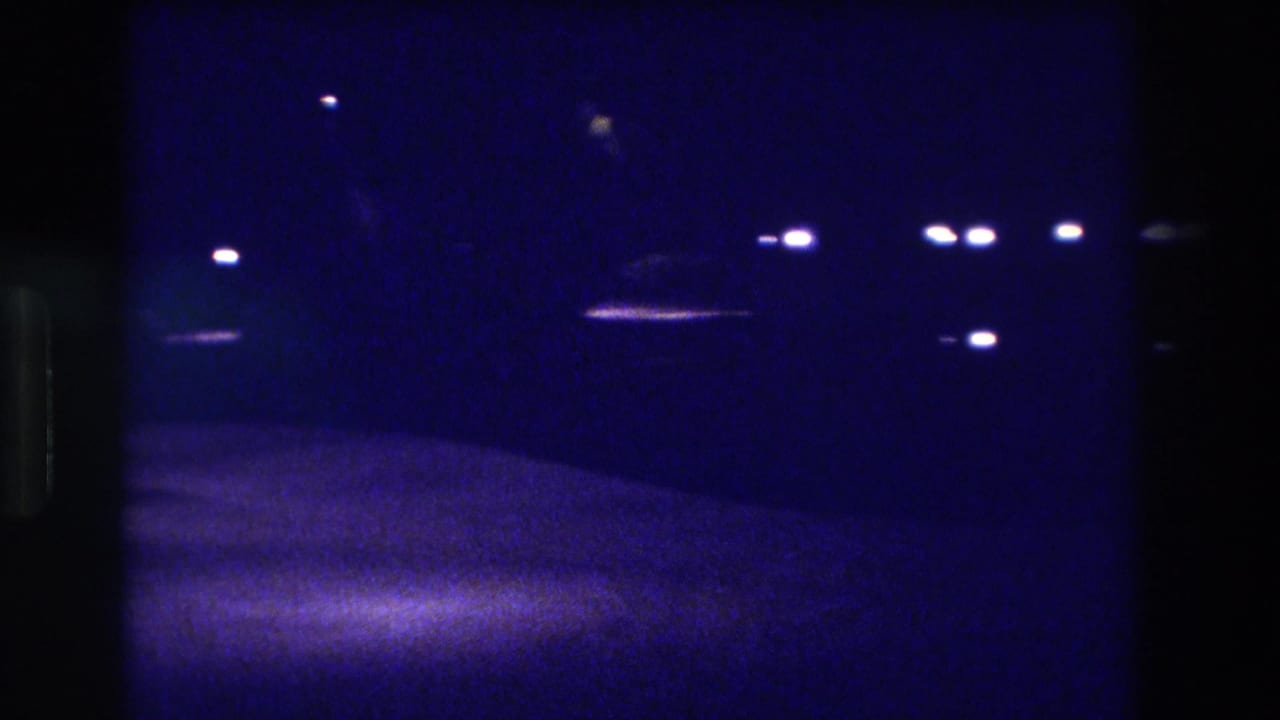 Handheld 8mm night shot of a dark street in Acapulco, Mexico, 1982, showing scattered overhead point lights and a motion-blurred road surface below.