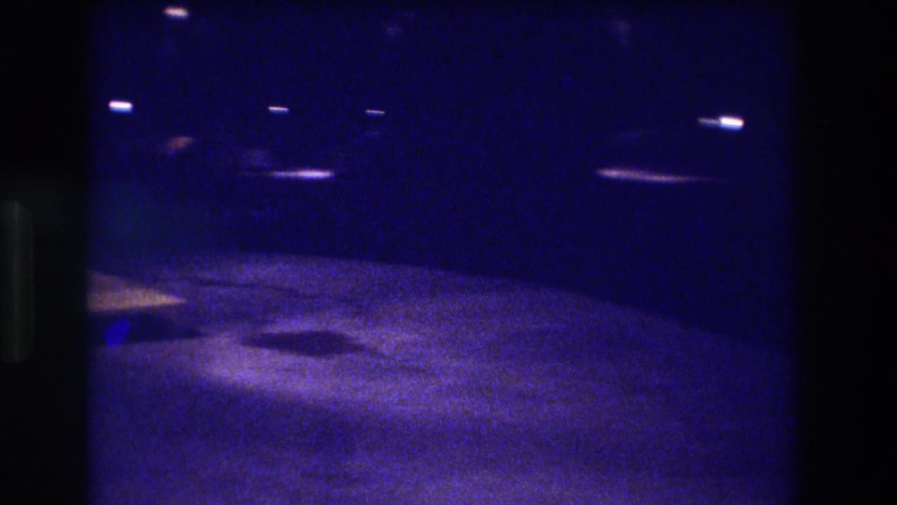 Low-light 8mm home movie frame from 1982, likely Acapulco — deep blue-indigo cast over dark road surface with scattered point-source lights.