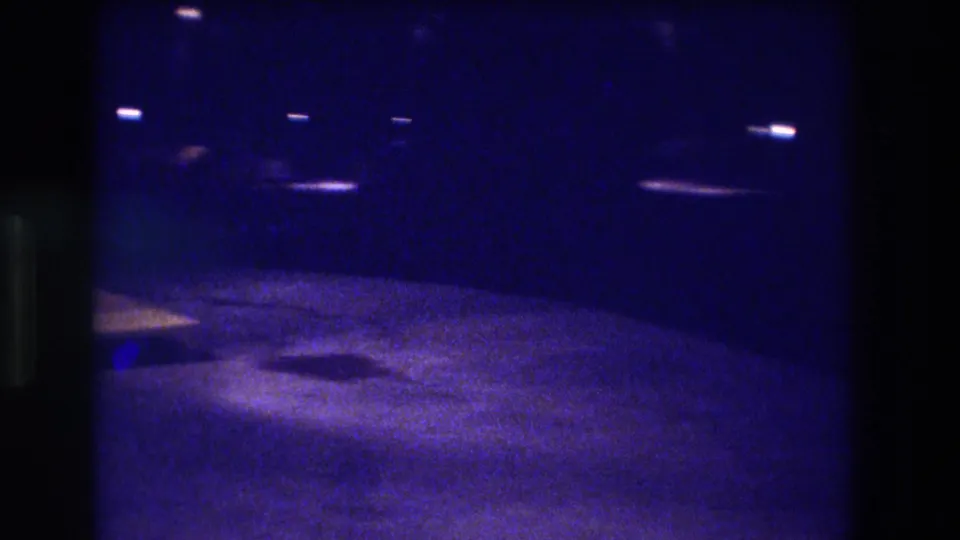 Low-light 8mm home movie frame from 1982, likely Acapulco — deep blue-indigo cast over dark road surface with scattered point-source lights.